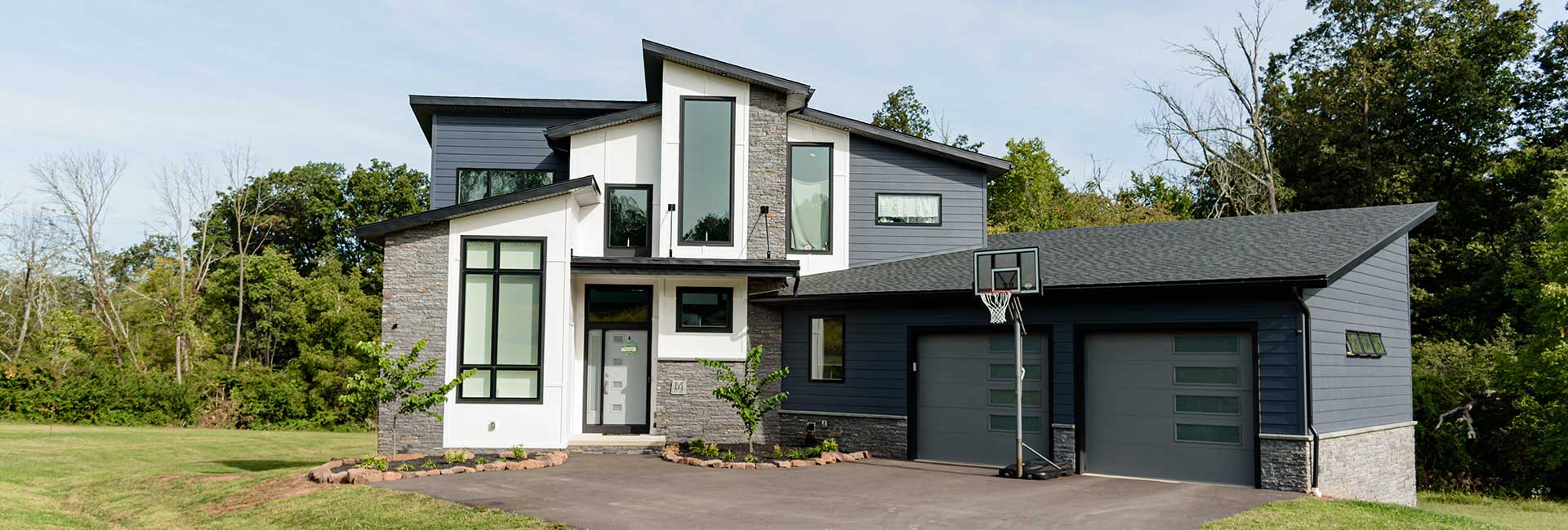 modern two-story house with dark gray and white exterior, large windows, stone accent, two car garage, and basketball hoop